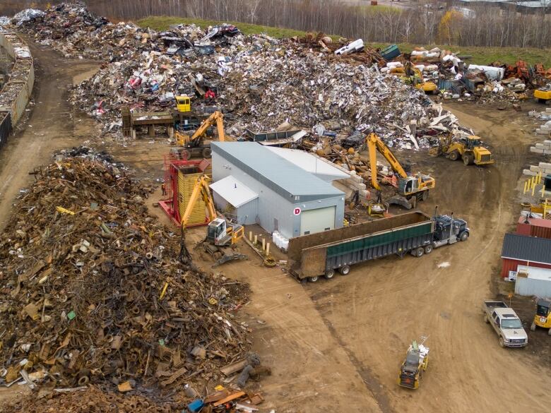 A small building surrounded by a pile of scrap material and heavy equipment.