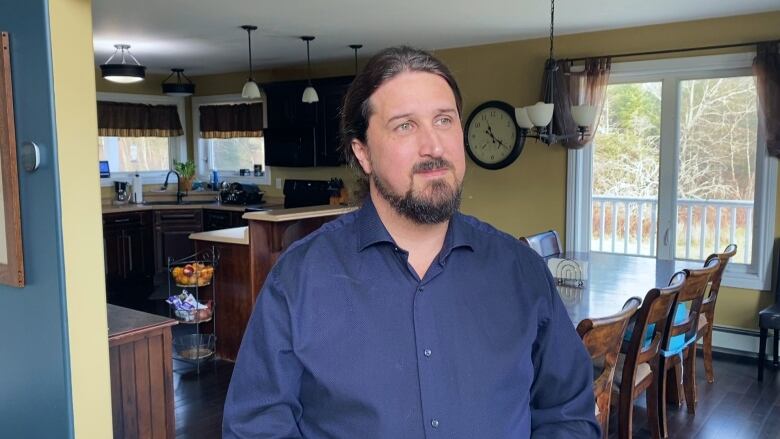 A man with a blue collared shirt and long dark hair stands in the entrance to a kitchen