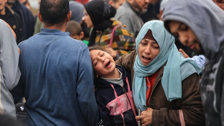 A crying child is carried by an adult through a crowd.