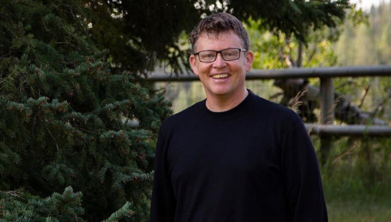 A man in a sweater stands in front of a tree.  