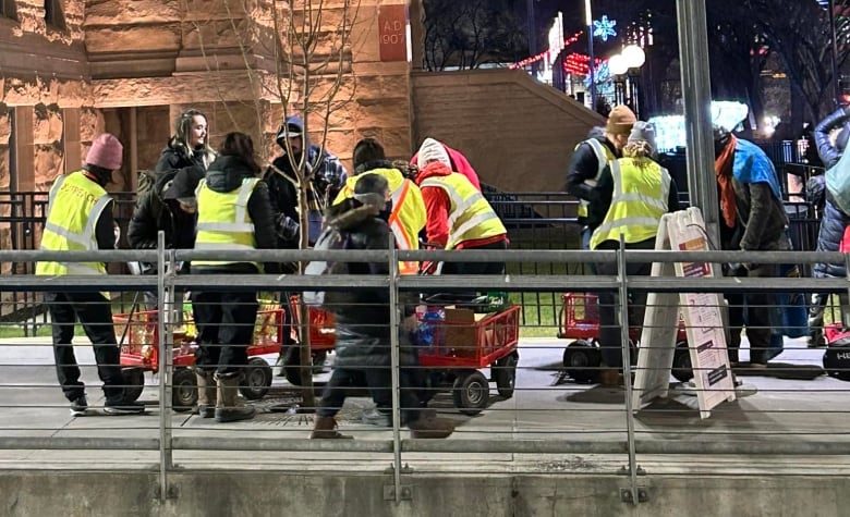 Men and women wear bright yellow construction vests and distribute food, clothing and other items  to the city's most vulnerable .