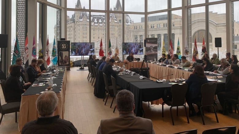 People are seen seated at large tables in a conference room with large windows looking out on some large old buildings.