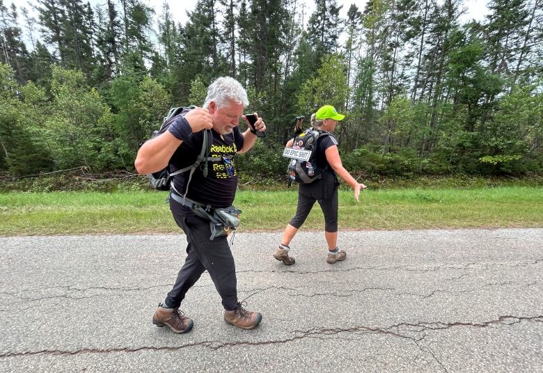 A man and a woman with backpacks walking along a quiet secondary road.