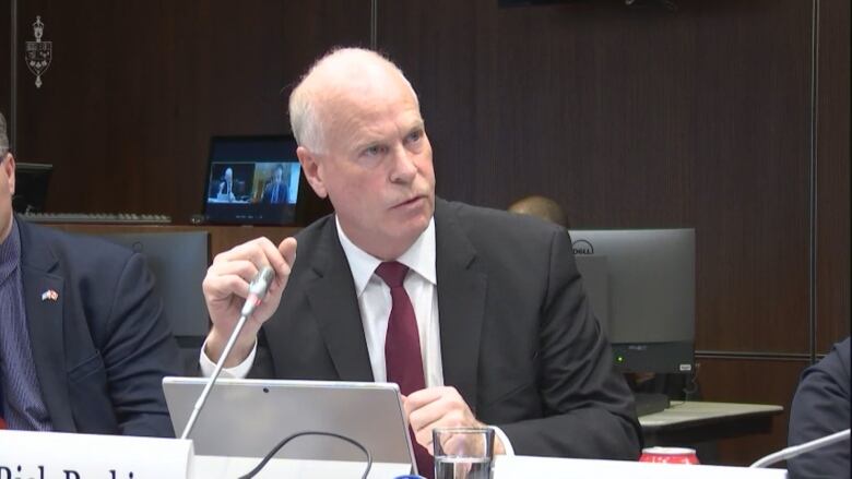 A man is seated at a table with a laptop and a microphone.