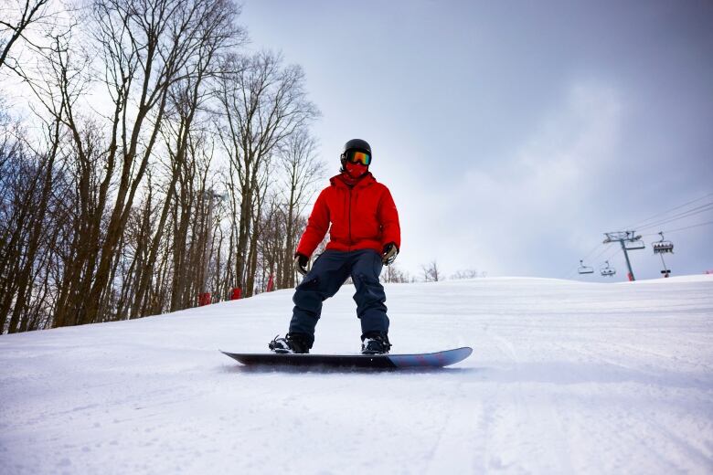 A man stands on a snowboard in a red jacket on a hill. 