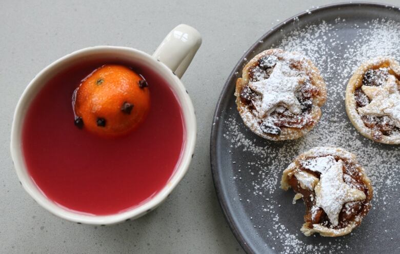 A drink with a mandarin orange in it. Next to it are tarts on a plate. 