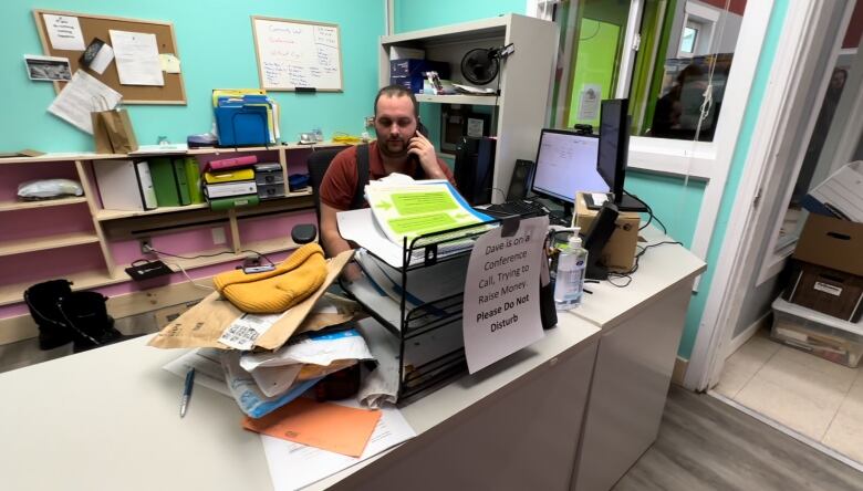 A man is on the phone at a desk in a crowded office.