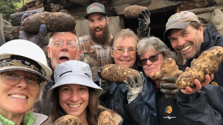 A group of smiling people hold up blackened potatoes in their hands.