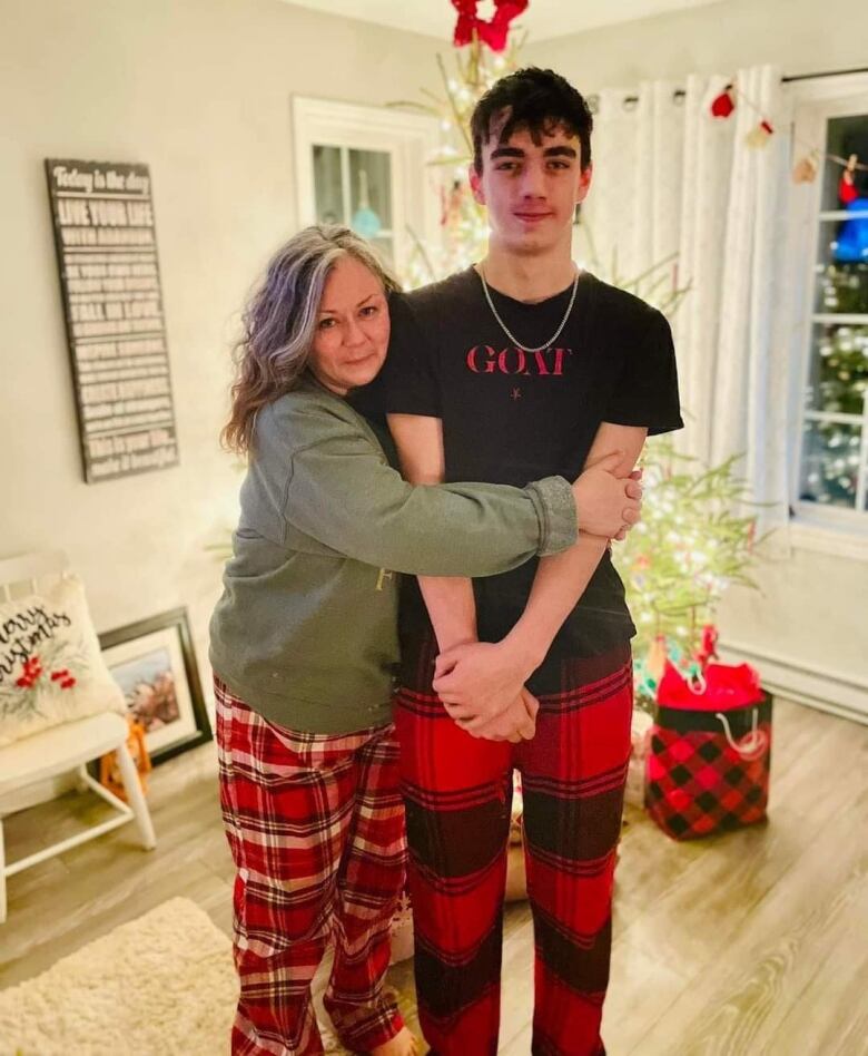 A woman is hugging her son, standing in front of a christmas tree. 