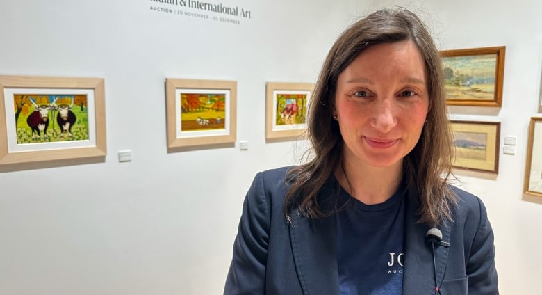 Woman standing in an art gallery in front of framed paintings. 