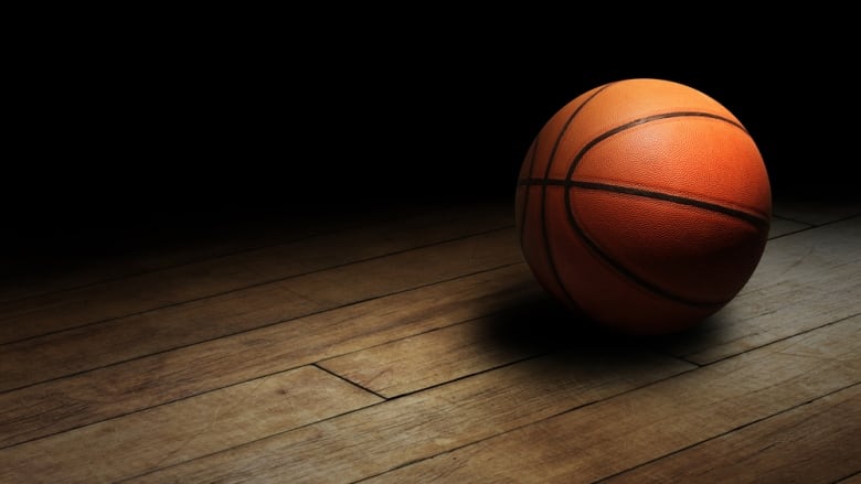 Basketball on hardwood floor with dark background.