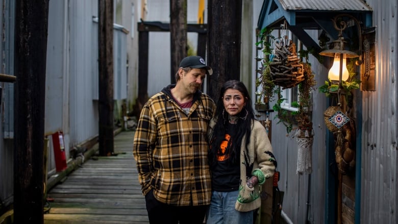 A couple stand outside a boat shed, looking sad.