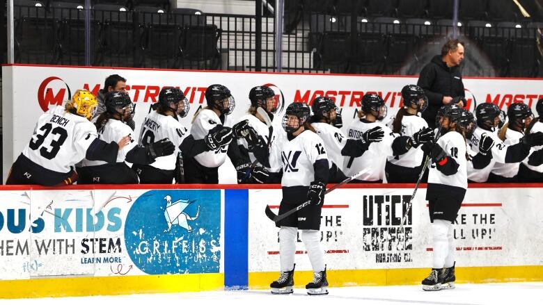 Two players in white jerseys, with a stylized W on them, skate on the ice past their bench, high fiving their teammates.