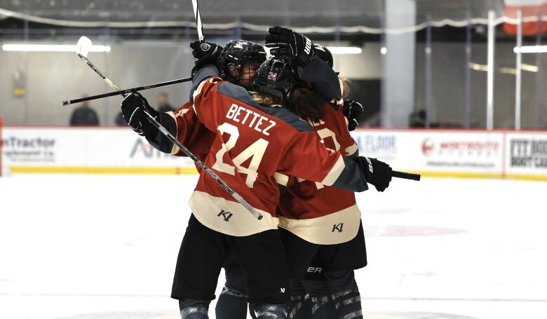 A group of female hockey players in maroon jerseys celebrate on the ice. Bettez is shown on the nameplate of one jersey.