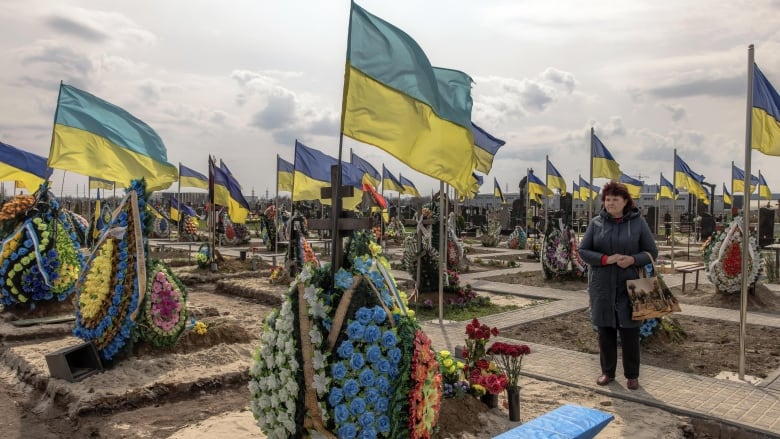 A woman stands in cemetery with many Ukrainian flags flying in the breeze.