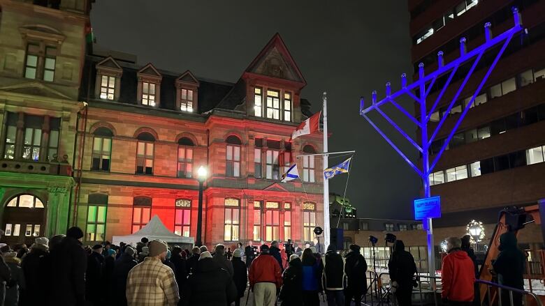 a crowd of people stand next to a large menorah in a public square. 