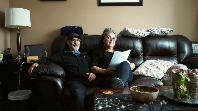 Two people sit on a couch in a living room. 