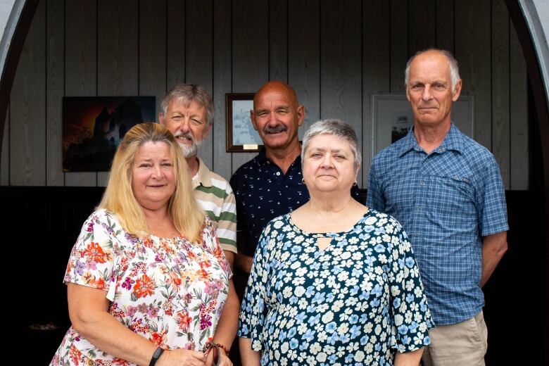 Five people stand in the doorway of a wooden church.