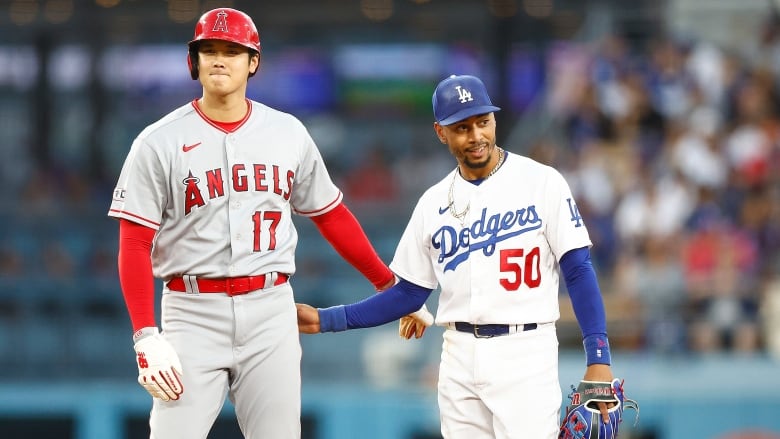 Two male baseball players from opposing teams stand next to each other during a game.