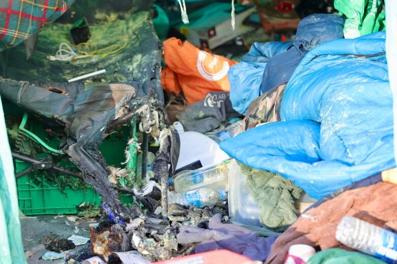 A sleeping cot, badly damaged by a fire, sits inside a tent, surrounded by sleeping bags and other items.