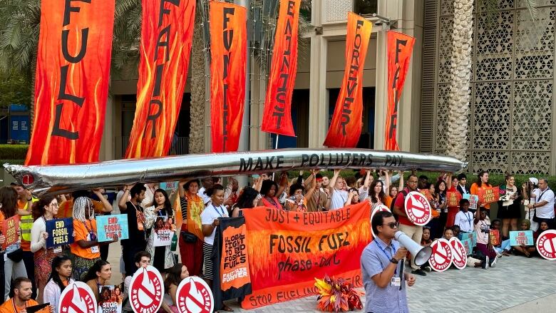 People hold up signs, banners, and a pretend pipeline as part of an anti-fossil fuel protest.