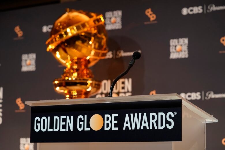 A podium with a microphone bears a sign that says Golden Globe Awards. A gold trophy can be seen in the background.