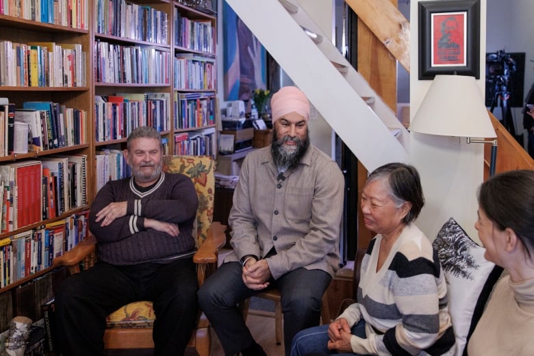 Four people sit and talk in a living room surrounded by a wall lined with books