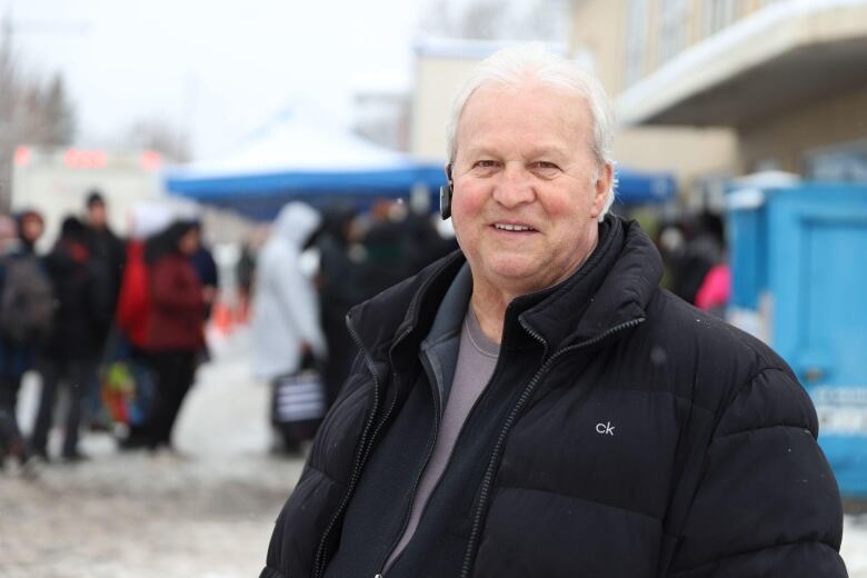 A man looks at the camera as he stands outside wearing a jacket 