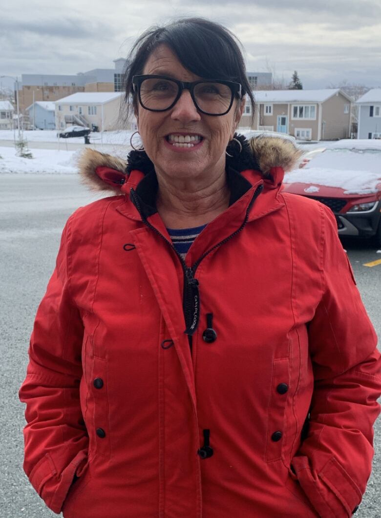 An elderly woman in a red winter jacket poses for a photograph