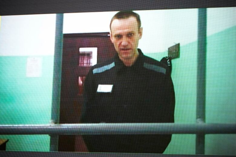 A lightly pixelated screen shows a man with a buzz cut standing behind bars.