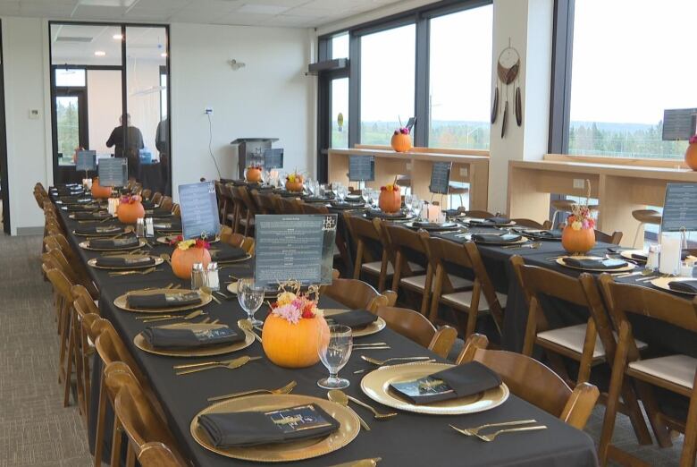 Two long tables lined with black tablecloth. They are decorated with pumpkins and gold plates. 