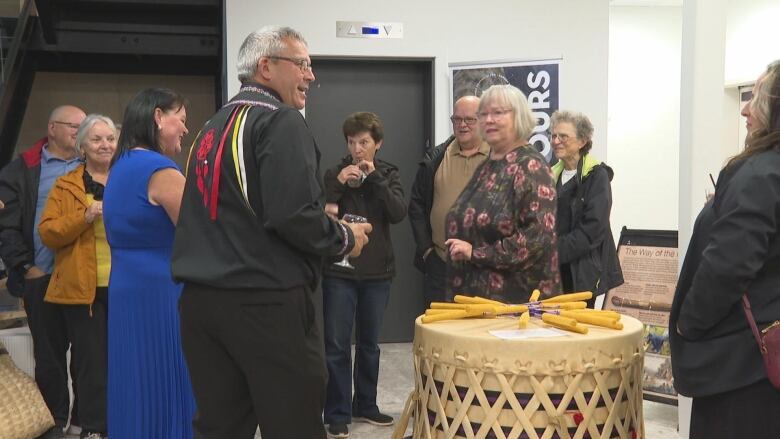 Chief Junior Gould mingles with people. There is a drum and people standing around. 