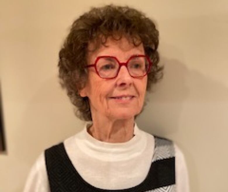 Older woman with grey hair and red glasses smiles 