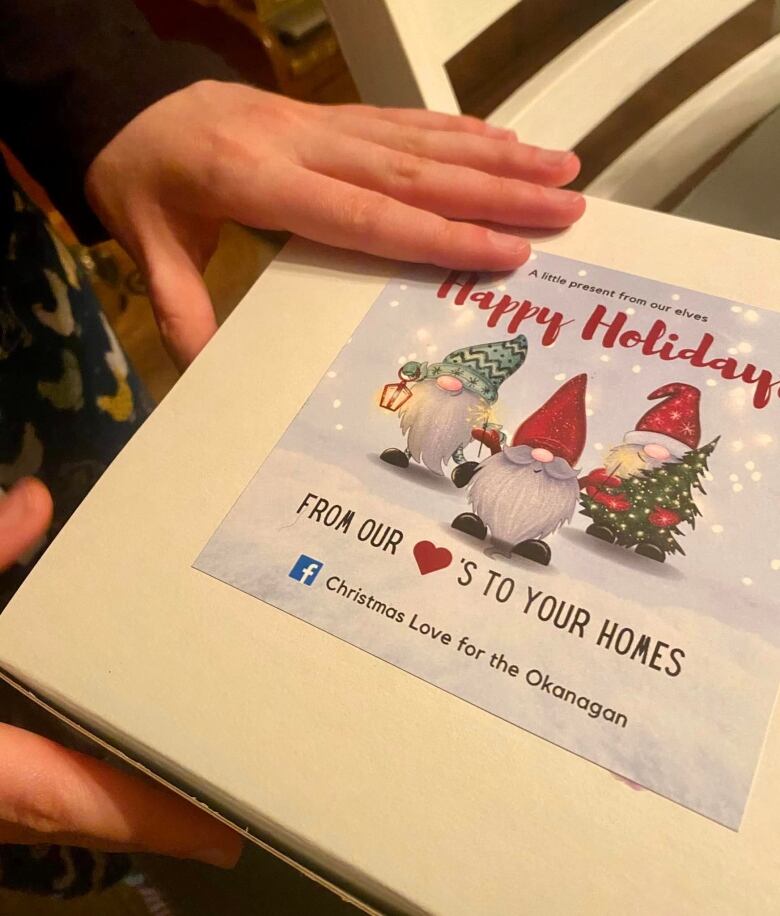 A hand holds a white box with pictures of Christmas elves on it.