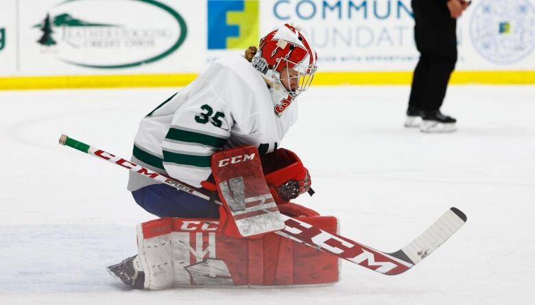 A female goaltender in a white jersey with red pads makes a save.