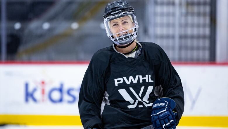 A female hockey player in a black jersey smiles on the ice.