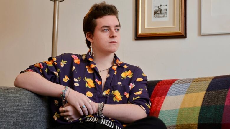 A person wearing a brightly-patterned shirt sits on a couch, leaning on the armrest.