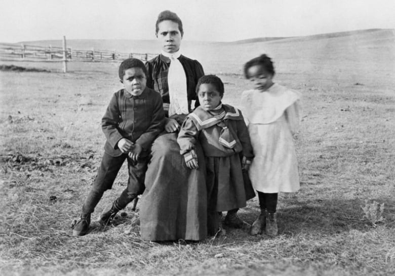 Black and white archival photo of one woman and three children sitting outside. 