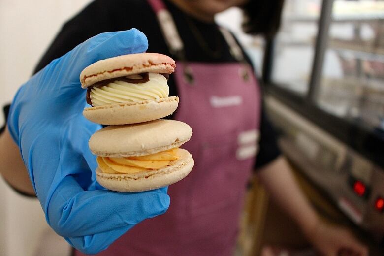 A gloved hand holds two macarons stacked on top of one another.