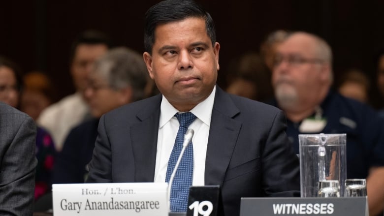 A minister in a suit seated at the witness desk preparing to testify.