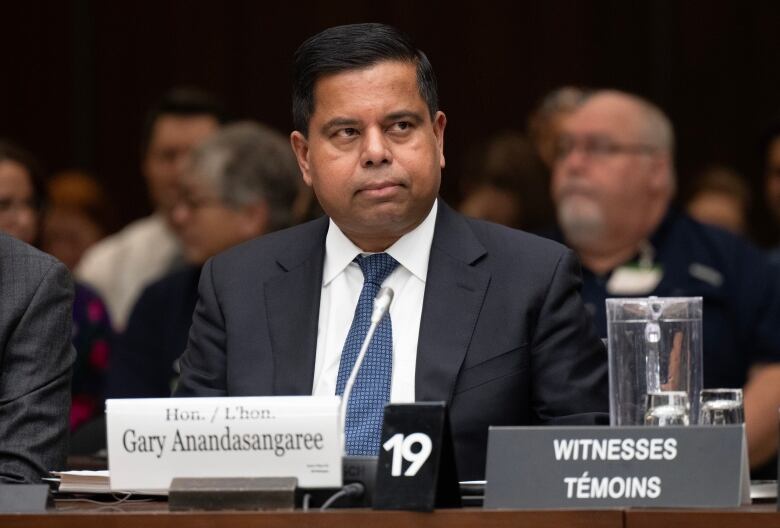 A minister in a suit seated at the witness desk preparing to testify.