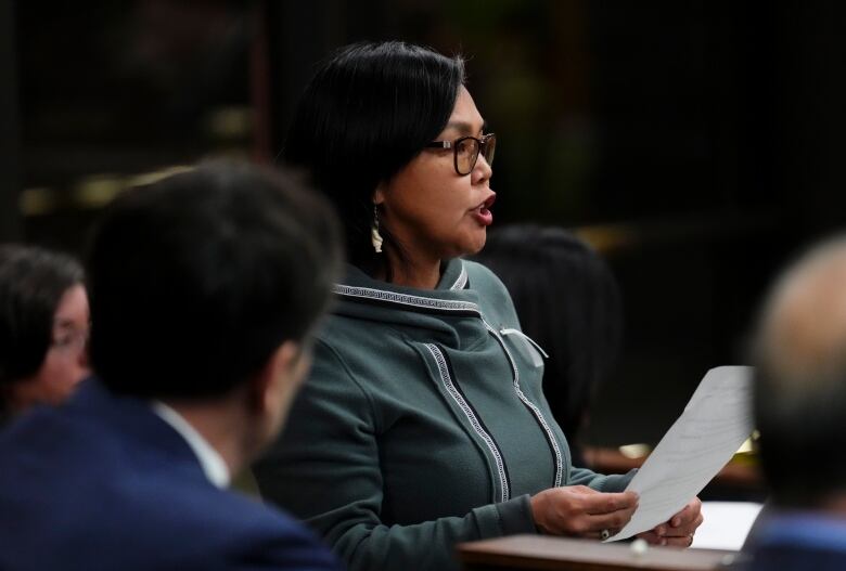 A woman, seen from the side, reads a question from a sheet in her hands.