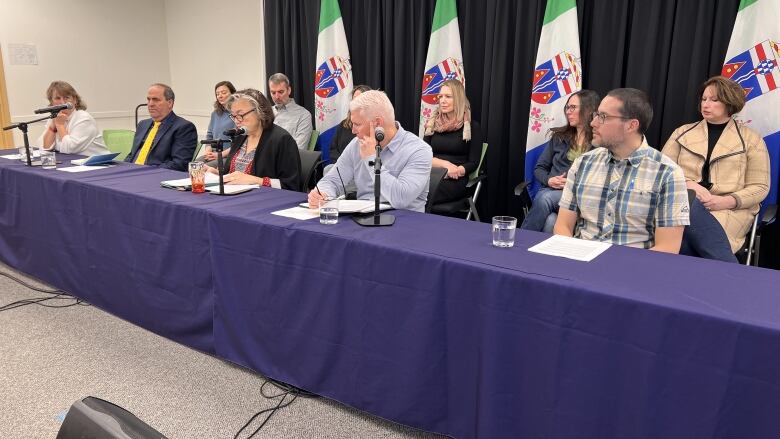 A group of people are seated behind a long table with microphones.