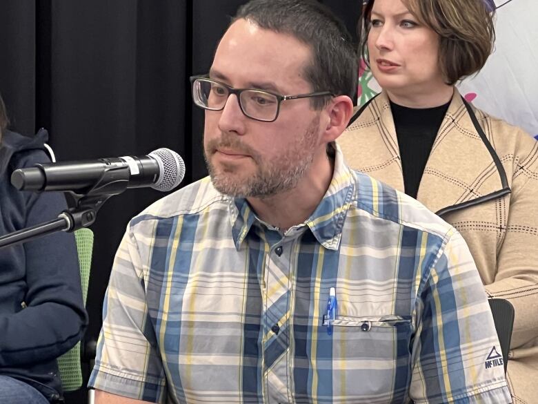 A man in checked shirt talks into a microphone.