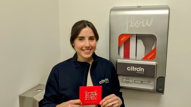 Someone stands next to a menstrual pad and tampon dispenser in a washroom.