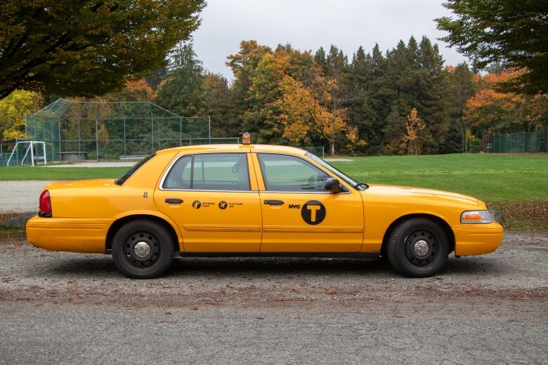 A yellow NYC cab is pictured park on the side of a park. 