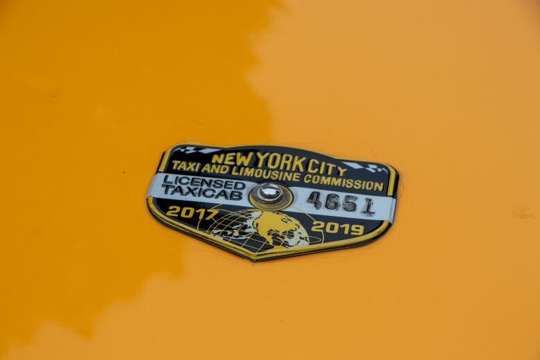 A close-up picture of a New York City taxi badge on a yellow background.