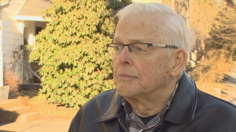 A senior with white hair and glasses looks at the camera.