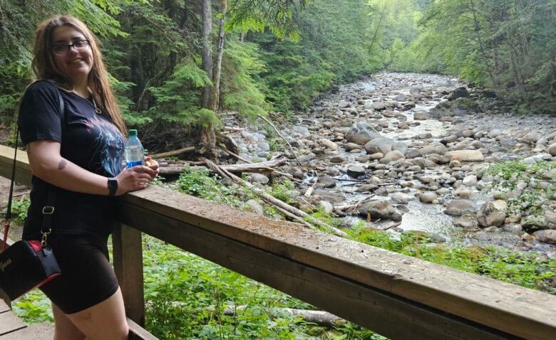 a woman stands next to a creek. 