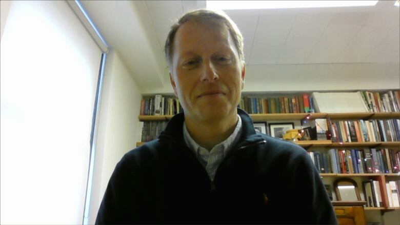 A smiling man wearing a sweater on a Zoom call.